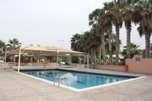 a swimming pool with palm trees and an umbrella at Bahrain Beach Bay in Az Zallāq