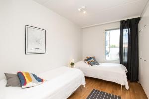 two beds in a white room with a window at Kotimaailma Two bedroom apartment with private sauna in Vaasa