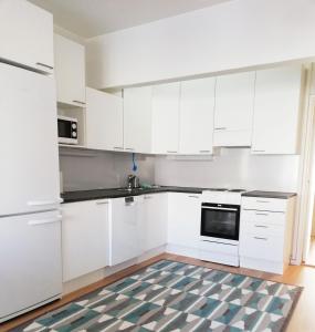 a white kitchen with white cabinets and a rug at Kotimaailma Family apartmen in the city center close to the beach in Vaasa