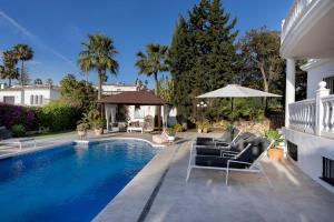 a swimming pool with chairs and an umbrella next to a house at Bed & Breakfast La Vida en Rosa in Marbella