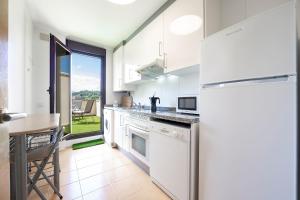 リャネスにあるApartamento Luz de Ponienteのテーブルと冷蔵庫のある白いキッチン