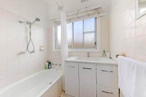 a white bathroom with a tub and a sink and a window at Sans Souci 4-Bedroom Home Near Beach in Sydney +9 photos
