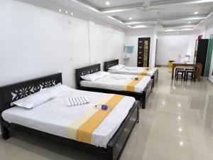 three beds in a room with a table and chairs at SR Residency in Kollam