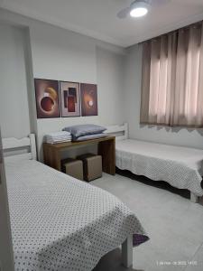 una camera da letto con due letti, un tavolo e una finestra di Excelente apartamento com vaga garagem a 50 metros da orla da Praia do Morro Guarapari a Guarapari