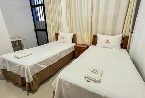 two beds in a hotel room with white sheets at Hospedaje El Emperador Talara in Talara