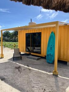 a yellow building with a surfboard next to a chair at Hotel Playa Los Angeles Bungalow Aloha in Ciudad del Carmen