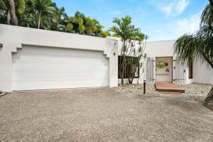 a white house with a garage and palm trees at Casa Del Sol Palm Cove in Palm Cove