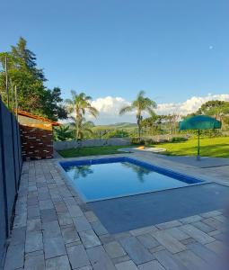 a swimming pool in a yard with an umbrella at Chácara Sitara Lazer e Eventos in Caldas