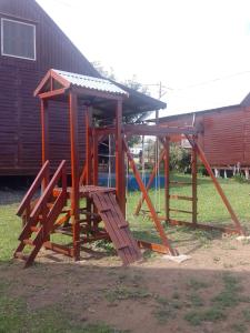 Un parque infantil con estructura de madera al lado de un granero. en Las Huellas Cabaña, en Balneario Pehuén-Có