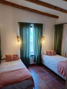 two beds in a room with green curtains and a window at La escondida las siringuillas in Tafí del Valle