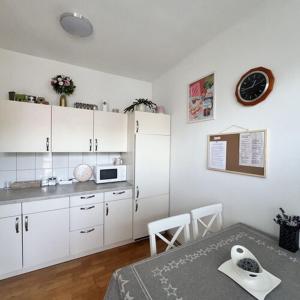 cocina con armarios blancos, mesa y reloj en Bem Apartman, en Gyenesdiás