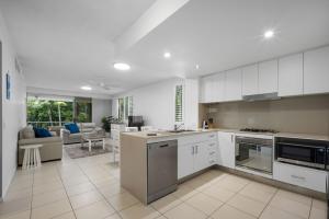 une cuisine avec des armoires blanches et un salon dans l'établissement Pool View 3-Bedroom Oasis in Drift Resort, à Casuarina