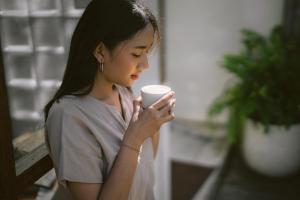 a woman sitting on a bench holding a cup of coffee at Ecozy Dijiwa Canggu in Canggu