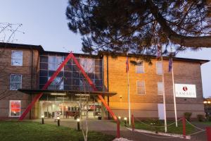 un edificio con un triángulo rojo delante de él en Ramada London Stansted Airport en Stansted Mountfitchet