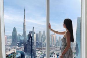 a woman looking out of a window at a city at Rose Rayhaan by Rotana - Dubai in Dubai