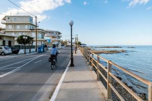 a person riding a bike on a sidewalk next to the water at GREEN n' BLUE apartments in Kalamaki