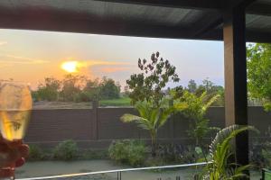 a person holding a wine glass looking out a window at the sunset at Private pool villa with rice field sunset views in Phum Pobos