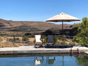 dos sillas y una sombrilla junto a una piscina de agua en Bloukrans Klein-bewarea Guest Farm, en Laingsburg