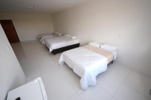 Cette chambre comprend 3 lits dans une chambre dotée de murs et de sols blancs. dans l'établissement Hotel Pedra Moura, à Vacaria 9 autres photos