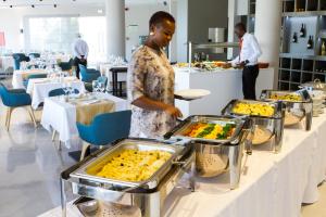 a man standing in front of a buffet line with trays of food at Montebelo Girassol Maputo Hotel in Maputo