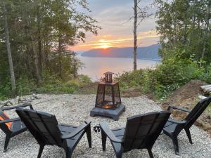 a group of chairs and a stove with a view of the water at YOURTE du FJORD in Sacré-Coeur-Saguenay