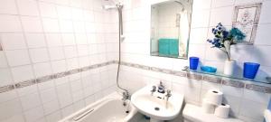 a white tiled bathroom with a sink and a bath tub at 9 Wheal Ramoth in Perranporth +6 photos