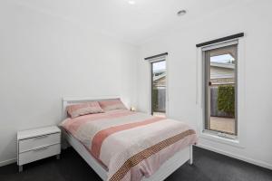 a white bedroom with a bed and two windows at Latte's Nest in Point Lonsdale