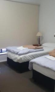 two beds in a room with a lamp on a table at Victoria room in Springvale