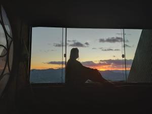 a person sitting in a window watching the sunset at Chalé canaã in Passa Quatro +18 photos