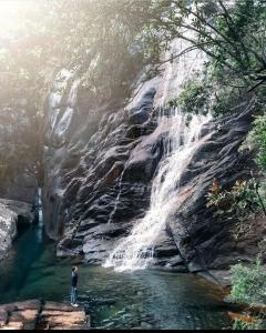 a man standing in the water next to a waterfall at Apê do NADINHO in Caparaó Velho