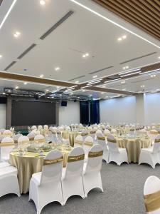 une salle de conférence avec des tables et des chaises blanches et un écran dans l'établissement Infinity Hotel, à Thái Bình