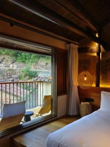 Schlafzimmer mit einem großen Fenster, einem Bett und einem Balkon in der Unterkunft Jiuli Countryside Boutique resort in Xinchang