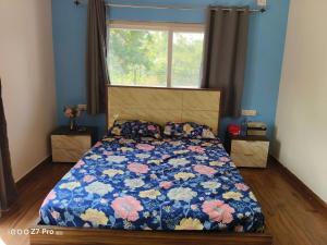 a bedroom with a bed with a floral comforter and a window at Huvazeel Villa - Murbad for Monthly rental only in Saralgaon