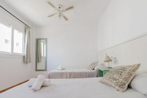 Un dormitorio blanco con dos camas y un ventilador de techo. en Apartamentos Timon - Emar Hotels, en Es Pujols
