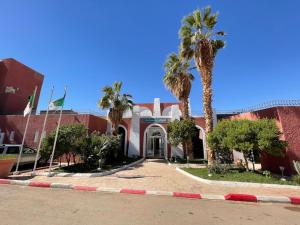 a building with palm trees in front of a street at Hotel Gourara in Timimoun
