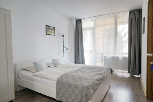 a white bedroom with a bed and a window at Tavaszház Apartmanok in Balatonfüred