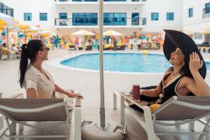 two women sitting in chairs by a pool at Golden Sands Suites in Dubai
