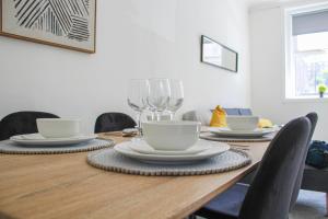 a wooden table with plates and wine glasses on it at 3-Bed Apartment - Near Clyde Shipyard - 25 min Glasgow Airport in Greenock +2 photos