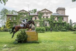 a man riding a horse jumping over a fence in front of a house at Pałac Baborówko in Szamotuły