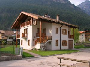 a white house with a balcony and mountains in the background at Appartamento Zorzi in Ziano di Fiemme