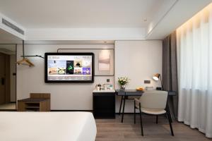 a room with a desk and a tv on the wall at Atour Hotel Qingdao Jinshatan Xiangjiang Road Subway Station in Huangdao