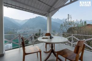 a table and chairs on a balcony with a view of mountains at Stayvista at Tulip Terraces Cozy Mountain Home with Fireplace in Manāli