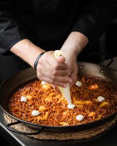 a person holding a wooden spoon in a pan of food at Hospes Amérigo, Alicante, a Member of Design Hotels in Alicante