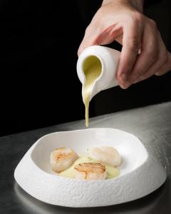 a person pouring sauce onto a plate of food at Hospes Amérigo, Alicante, a Member of Design Hotels in Alicante