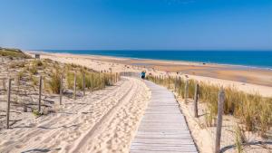 Maison dans la Pinède à Lacanau في لاكانو: مسار خشبي يؤدي إلى شاطئ عليه أشخاص