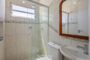 a bathroom with a sink and a toilet and a mirror at Apto Vista Mar 3Q e Garagem 130m da Praia ROR0002 in Bombas