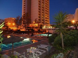 a pool with chairs and umbrellas in a city at night at Apartamentos Turisticos Perola da Rocha in Portimão