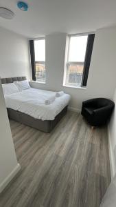 a bedroom with a bed and a chair and two windows at 2 Bed Sizeable Station House Apartment - Free Wifi, Parking & EV in Scunthorpe