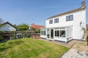 une cour arrière avec une maison blanche avec une pelouse dans l'établissement Sanderlings by Winterton Cottages, à Winterton-on-Sea