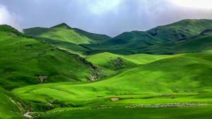 Un campo verde con montañas al fondo en Olive Eco Village Hotel, en Pārtol